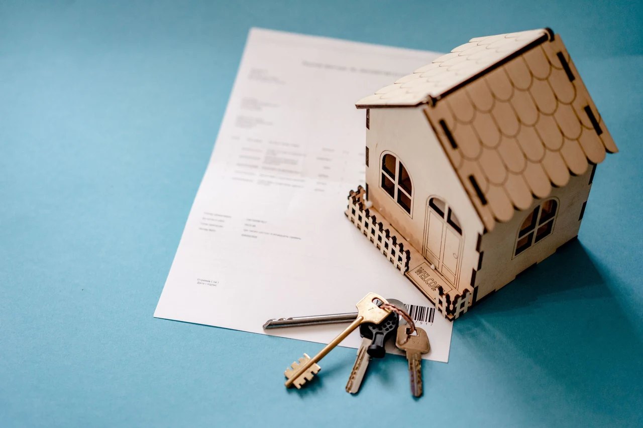 Property documents and keys beside a wooden house model